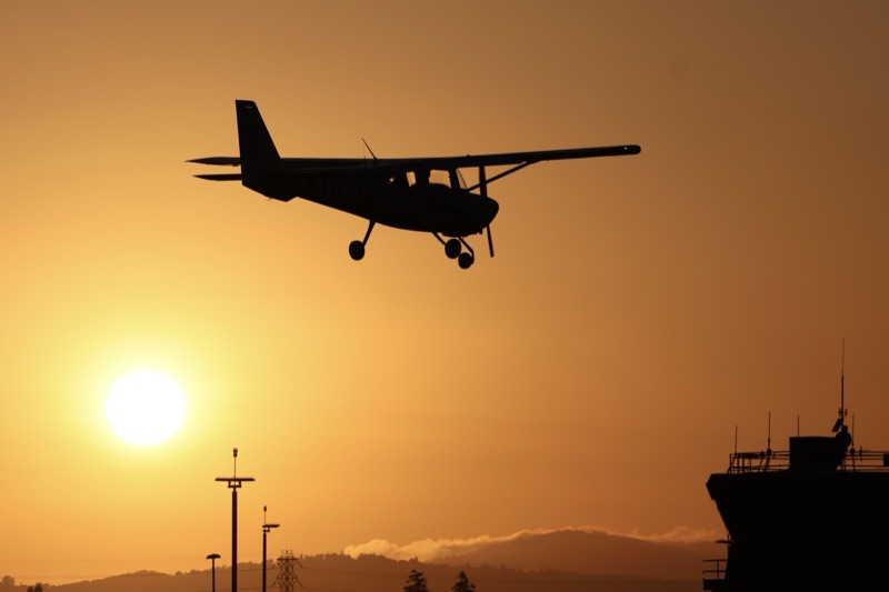 Cessna silhouetted on final approach against an orange sunset